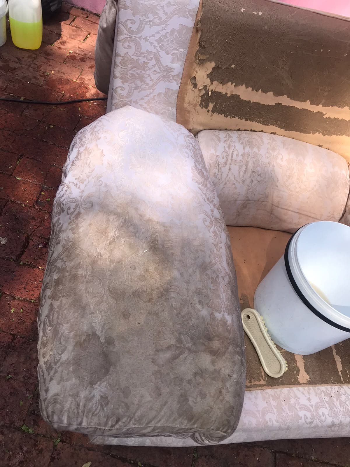 Soiled patterned armchair upholstery beside a bucket and brush, with damaged backing exposed.