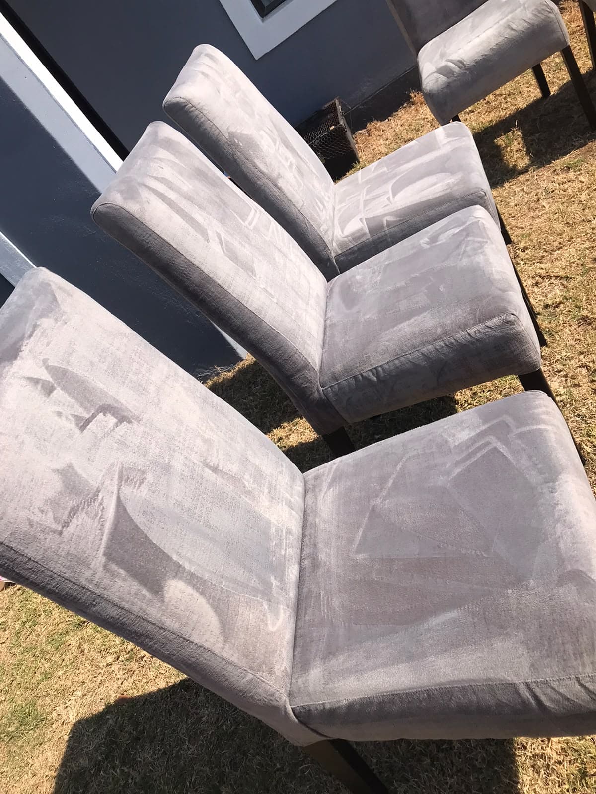 Grey upholstered dining chairs standing outdoors, with cleaning passes visible in the fabric.
